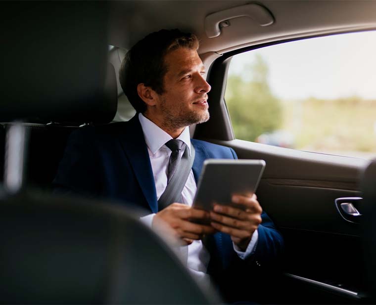 Man in a suit enjoys a comfortable ride in a limo car while using a tablet.