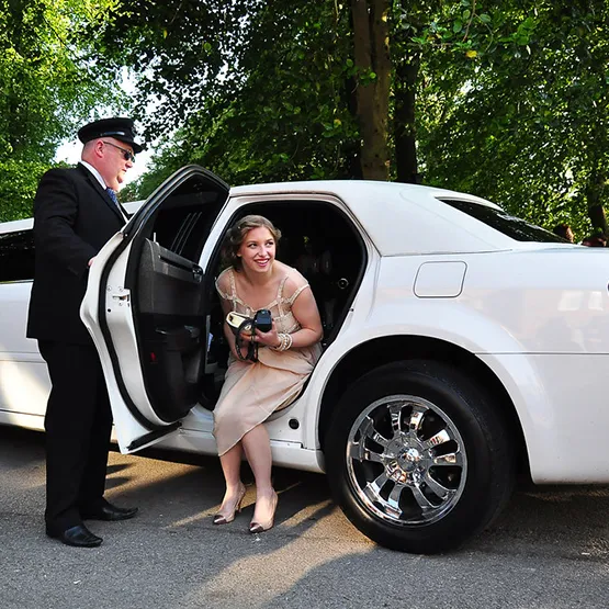 Limousine driver helps a guest get out of a nice white car for a special event.